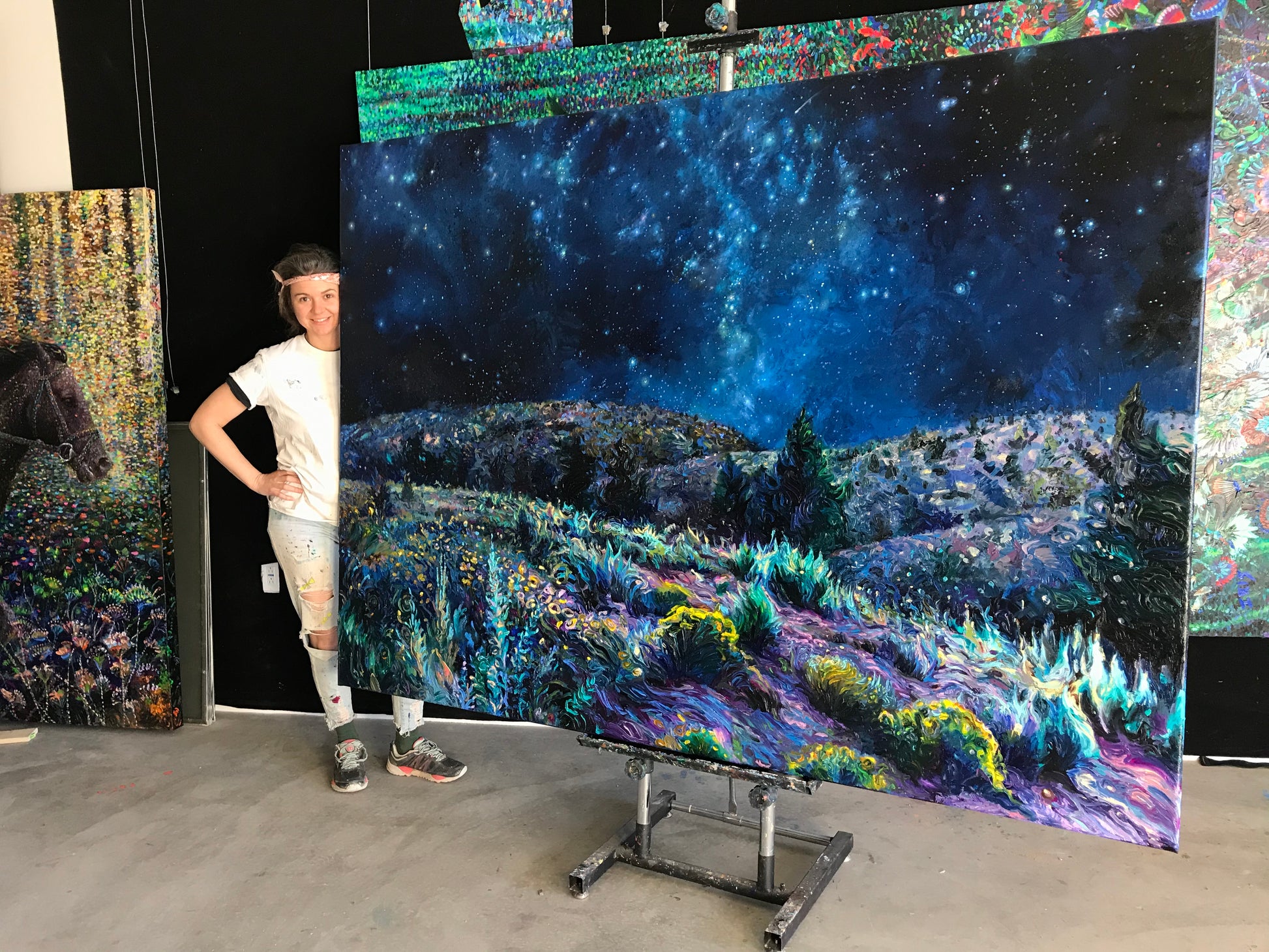 Iris Scott standing beside the Sage and Time desert night sky canvas print featuring a glowing New Mexico landscape and vibrant Milky Way artwork